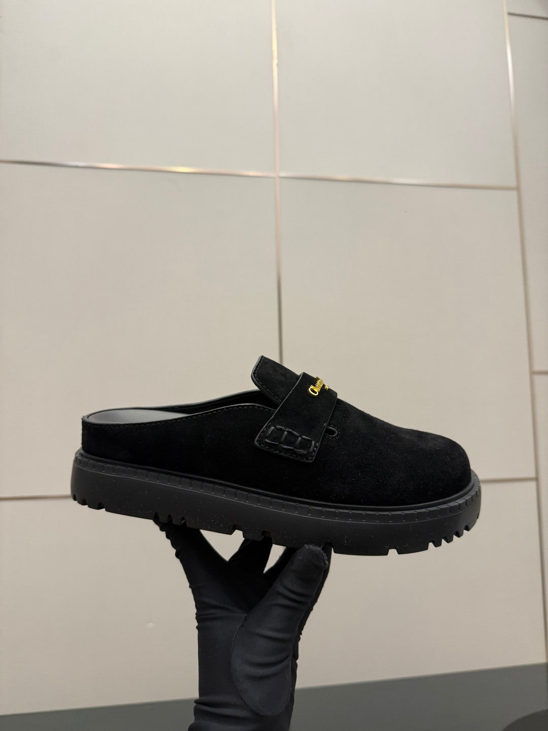 Black suede mule with strap and gold buckle detail, chunky tread sole