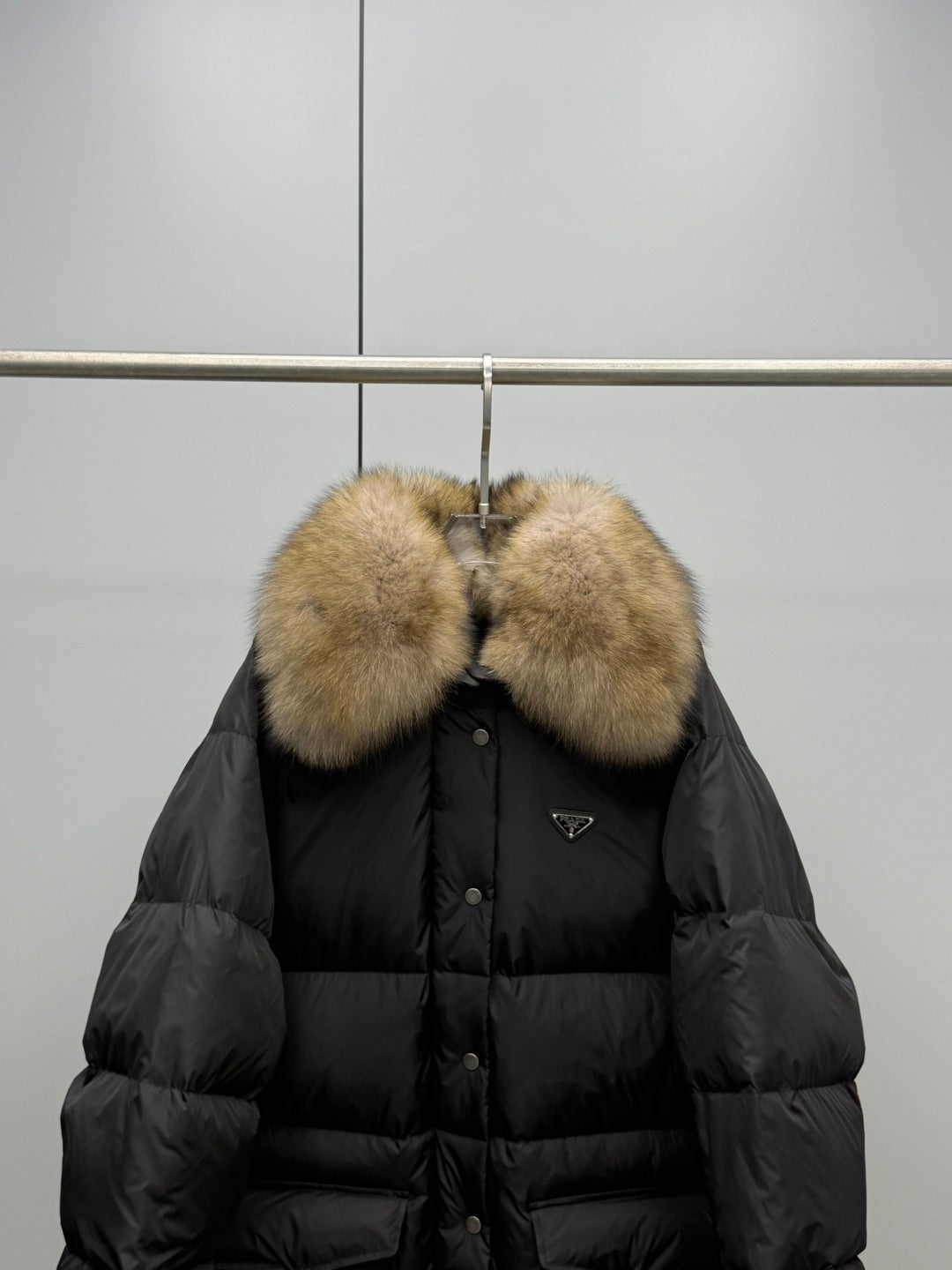 Black puffer jacket front with tan fur collar and triangular logo patch