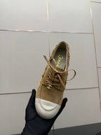 Ladies tan suede sneaker held in hand, lace-up front with white toe cap