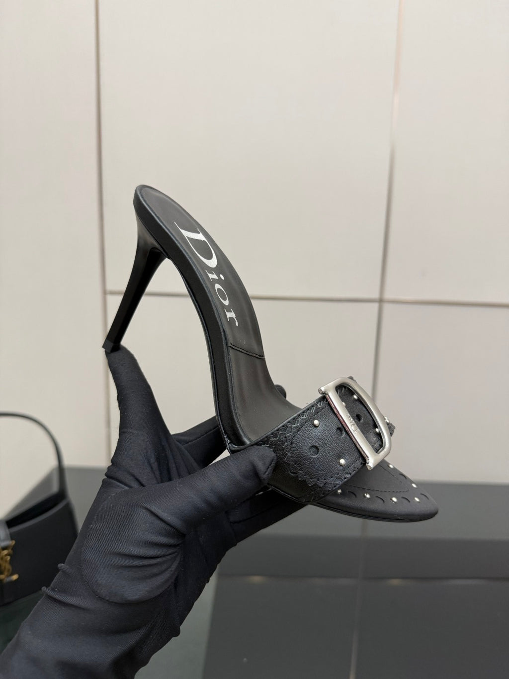Black studded mule sandal with silver buckle strap held in hand
