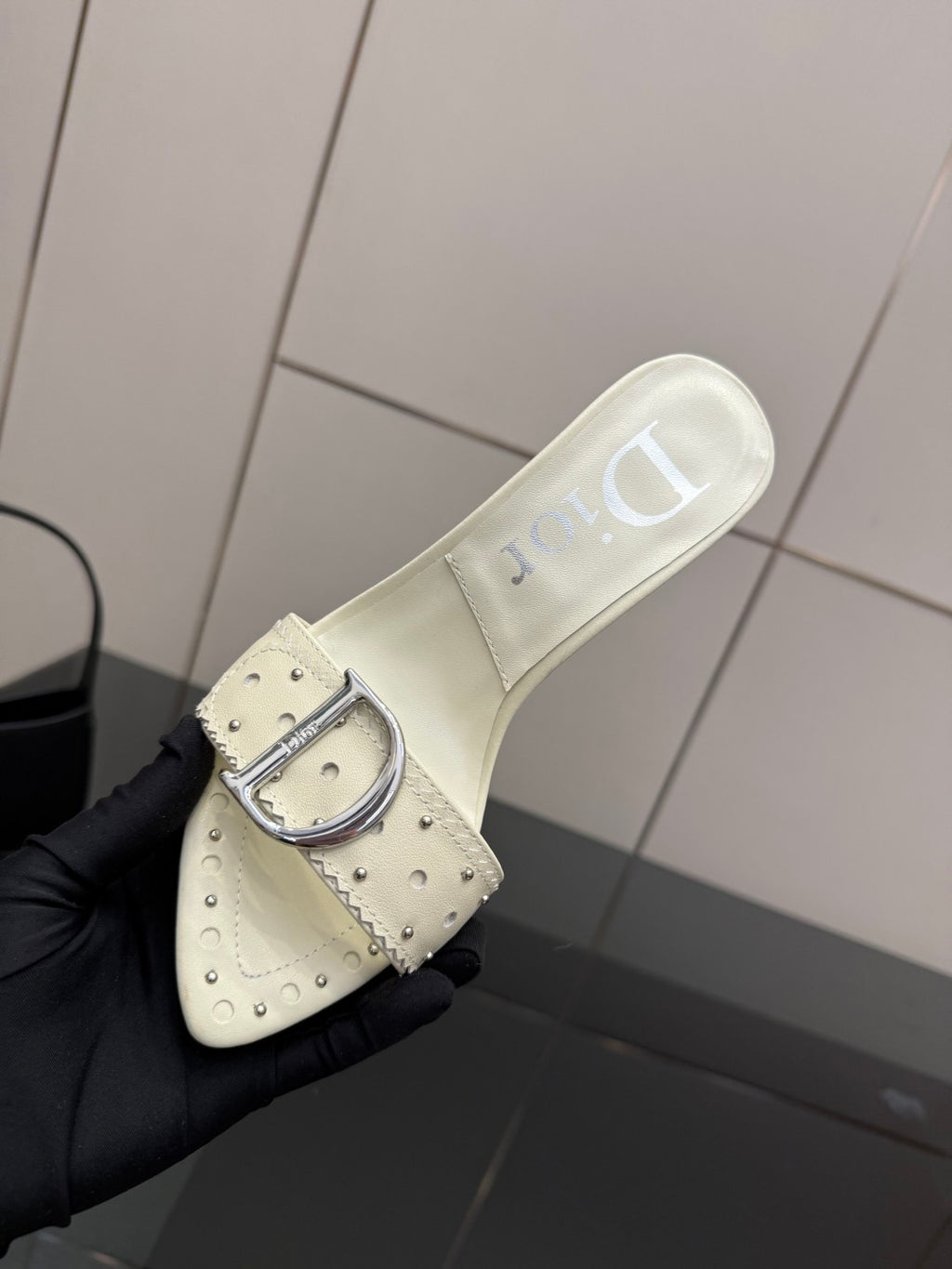 Dior ladies cream mule with metal buckle strap, close-up on black glove