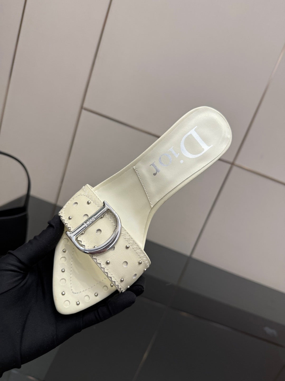 Dior ladies cream mule with metal buckle strap, close-up on black glove