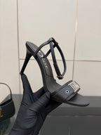 Black leather heeled sandal held in hand; thin straps and Dior label.
