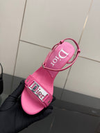 Pink Dior ladies heeled sandal with ankle strap and buckle, sole-up view in hand.
