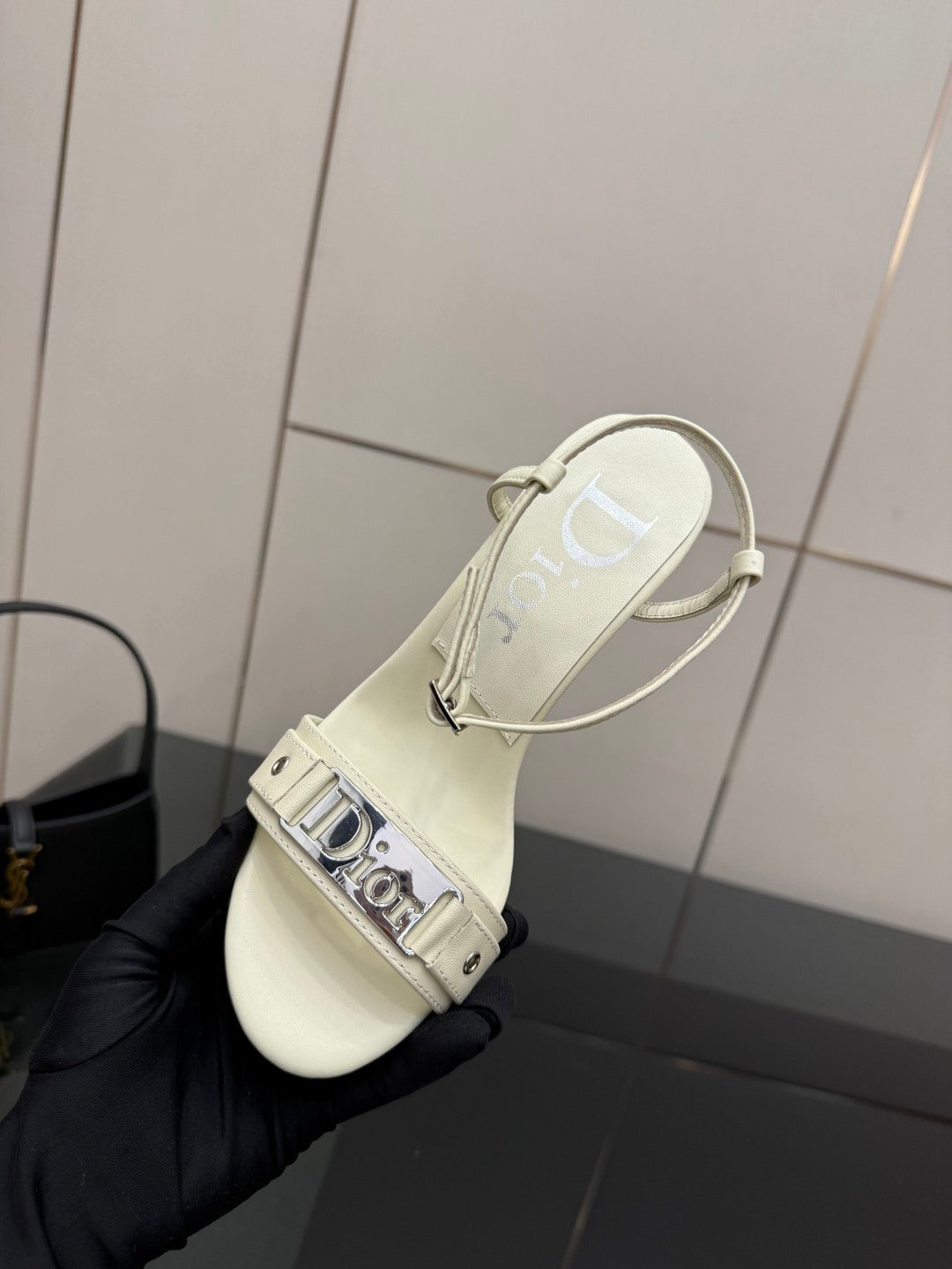 Cream slingback sandals held in black gloves, ankle strap with Dior logo