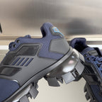 Prada unisex sneaker close-up with dark blue upper, gray heel panel, and spiked outsole