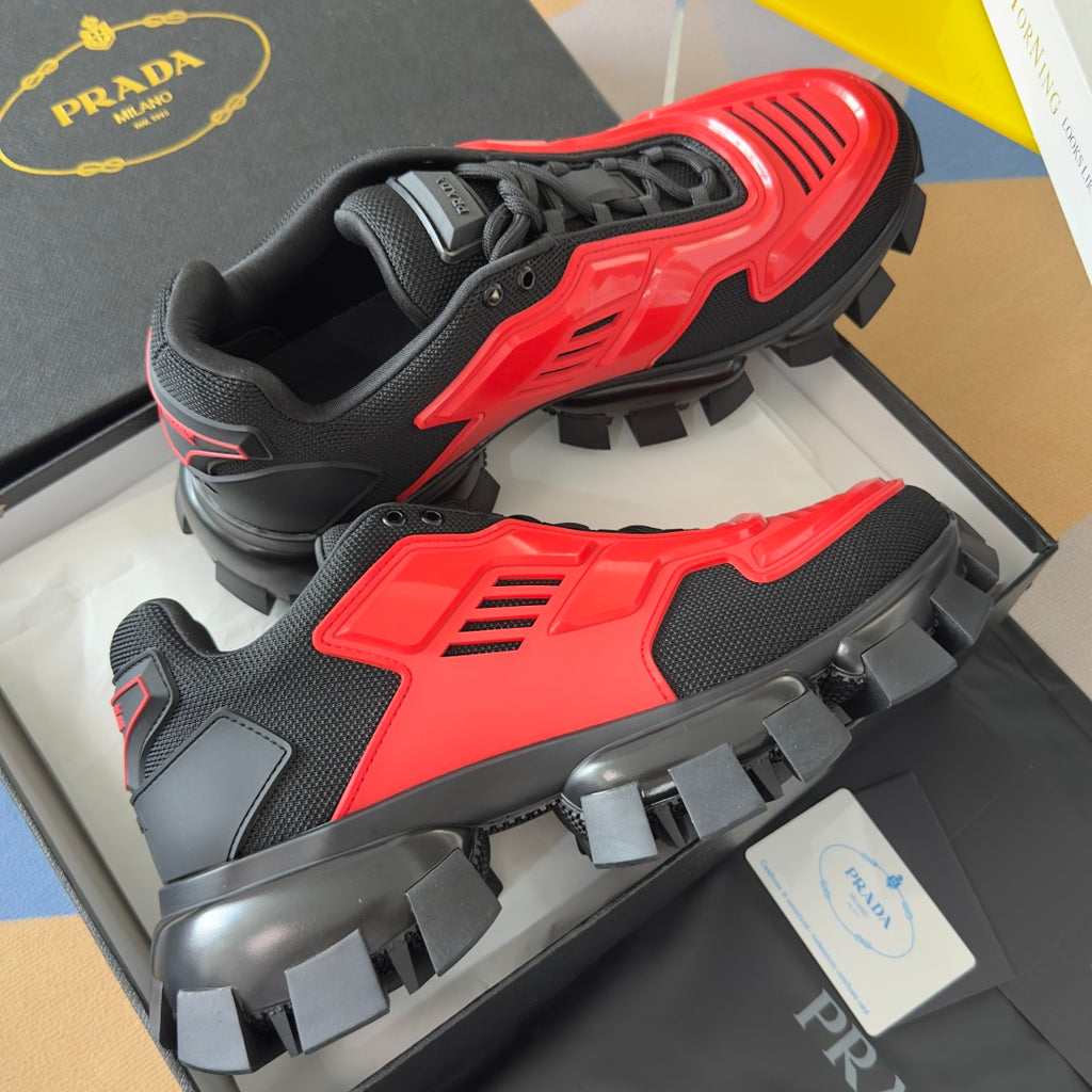 Unisex Prada sneakers with red and black panels, lace-up, and oversized studded outsole.