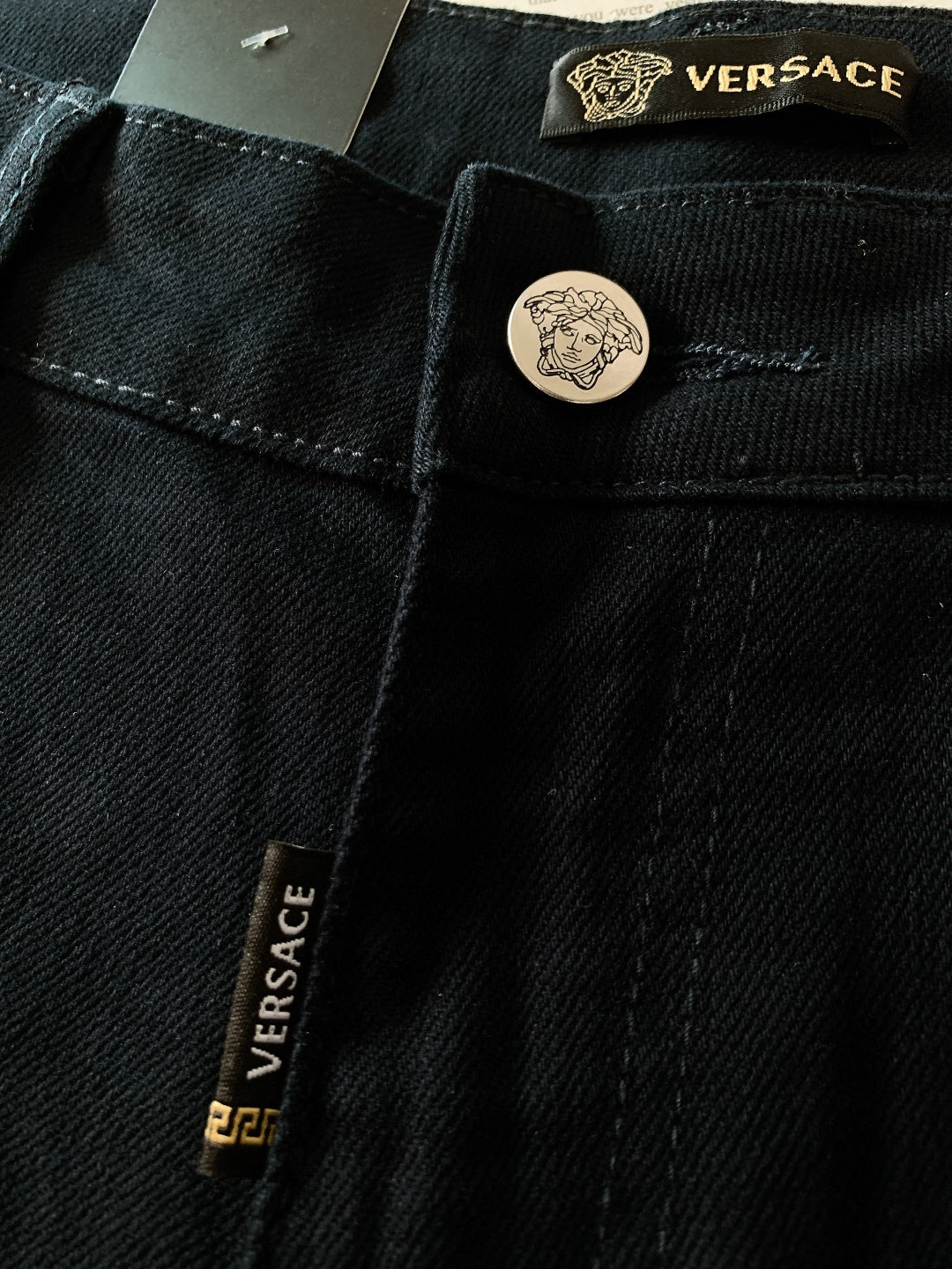 Black denim jeans with Versace label and round engraved button