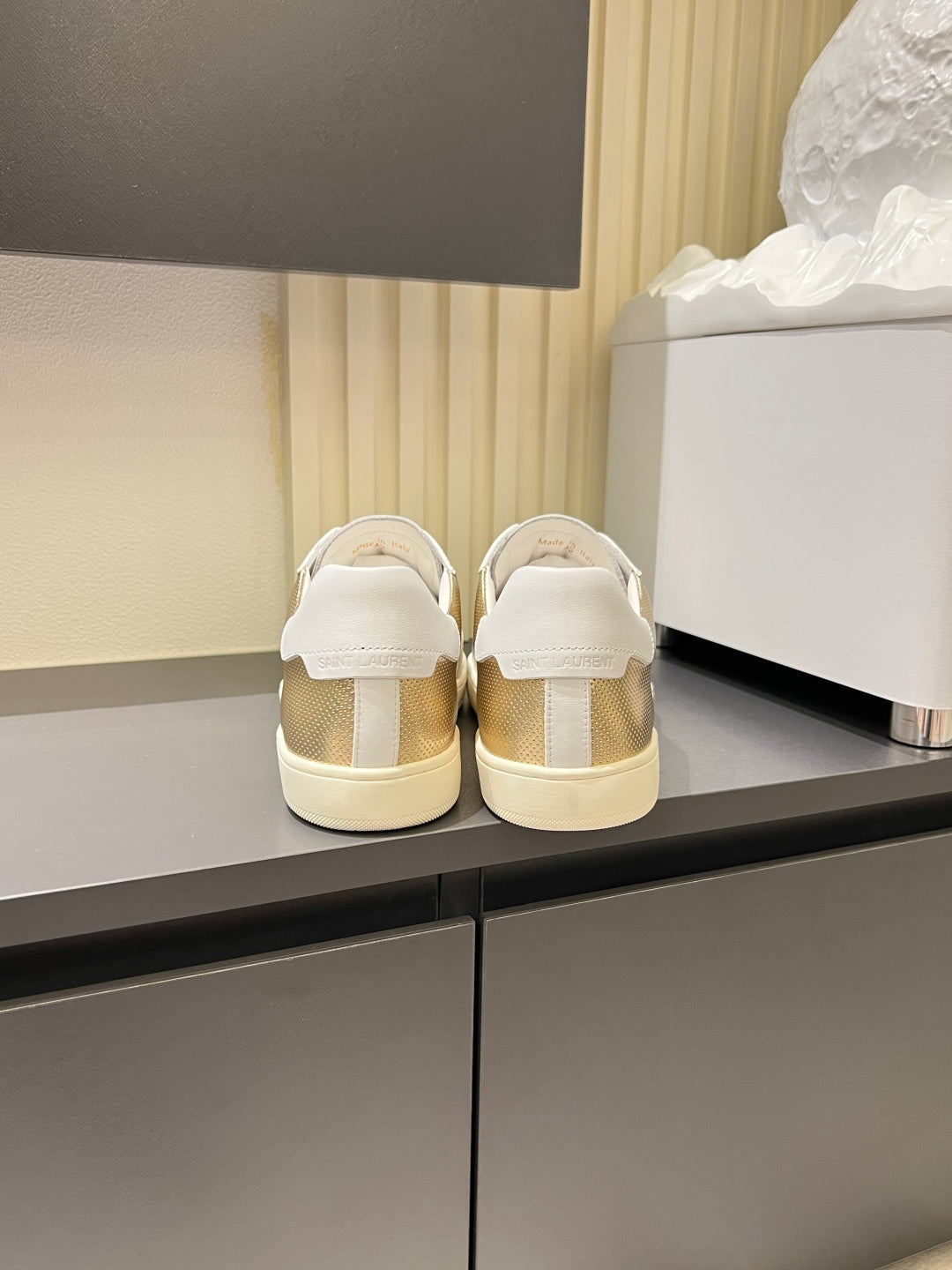 Pair of low-top sneakers, white heel and gold mesh upper, rear view with soles visible
