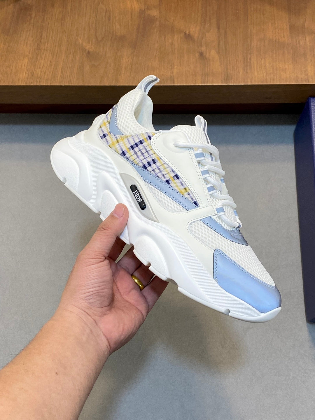 White and light blue lace-up sneakers with plaid trim, held in hand