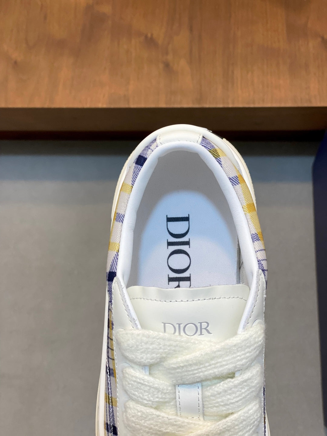 White sneaker upper with Dior label on tongue and blue plaid collar trim.