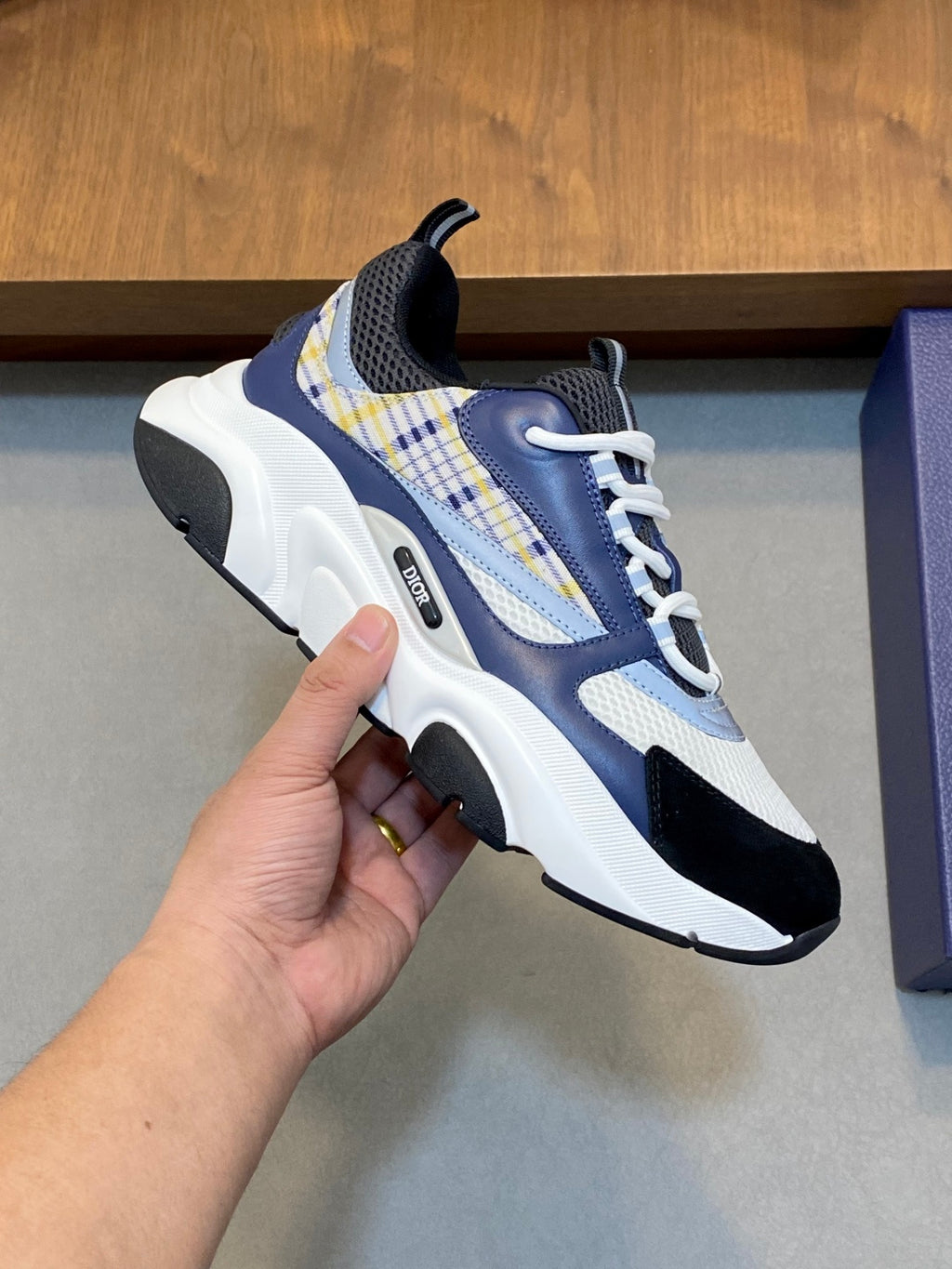 Dior unisex sneaker close-up held in hand; blue and white mesh with plaid strap