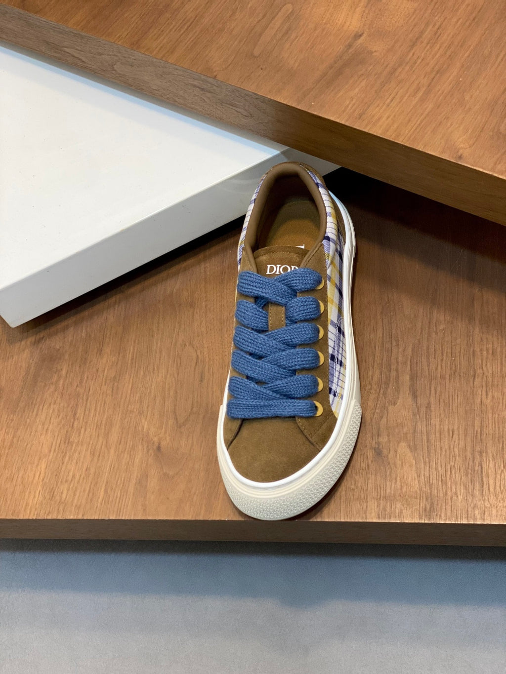 Single low-top sneaker on display with blue laces, plaid sides, and white rubber sole.