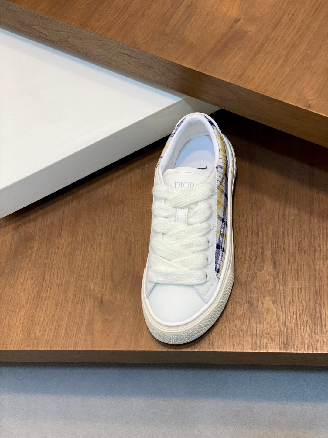 White lace-up low-top sneaker with blue plaid lining visible at heel.