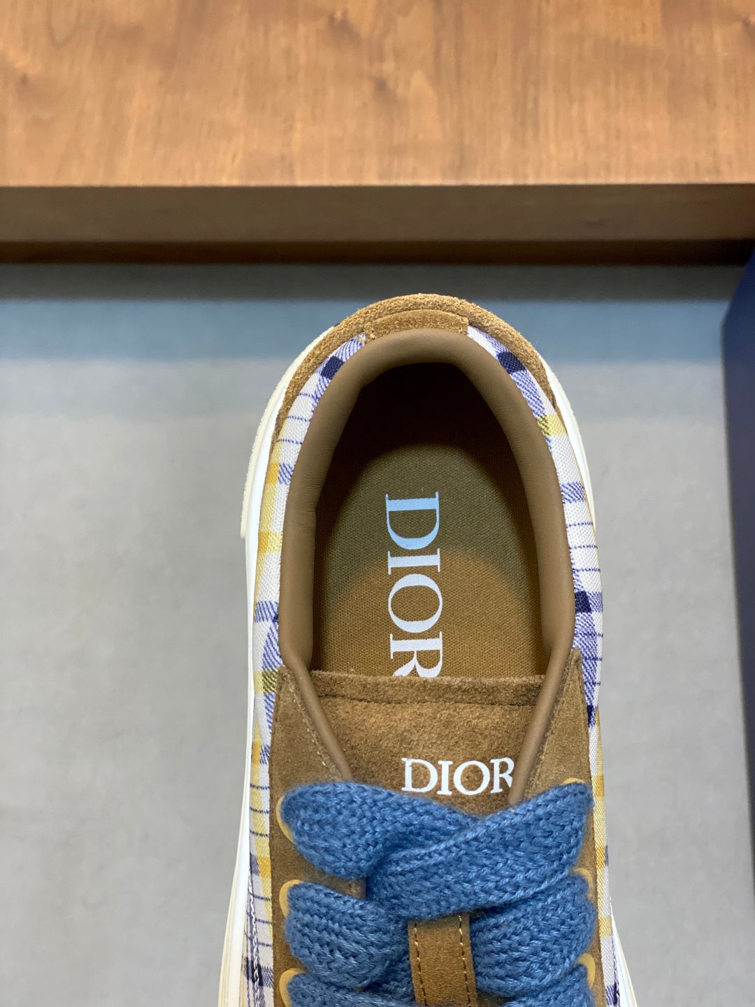 Close-up of low-top sneaker tongue with blue laces and Dior logo, brown suede collar.