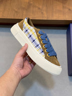Close-up of low-top sneaker showing blue lace-up with plaid panel and white sole edge.