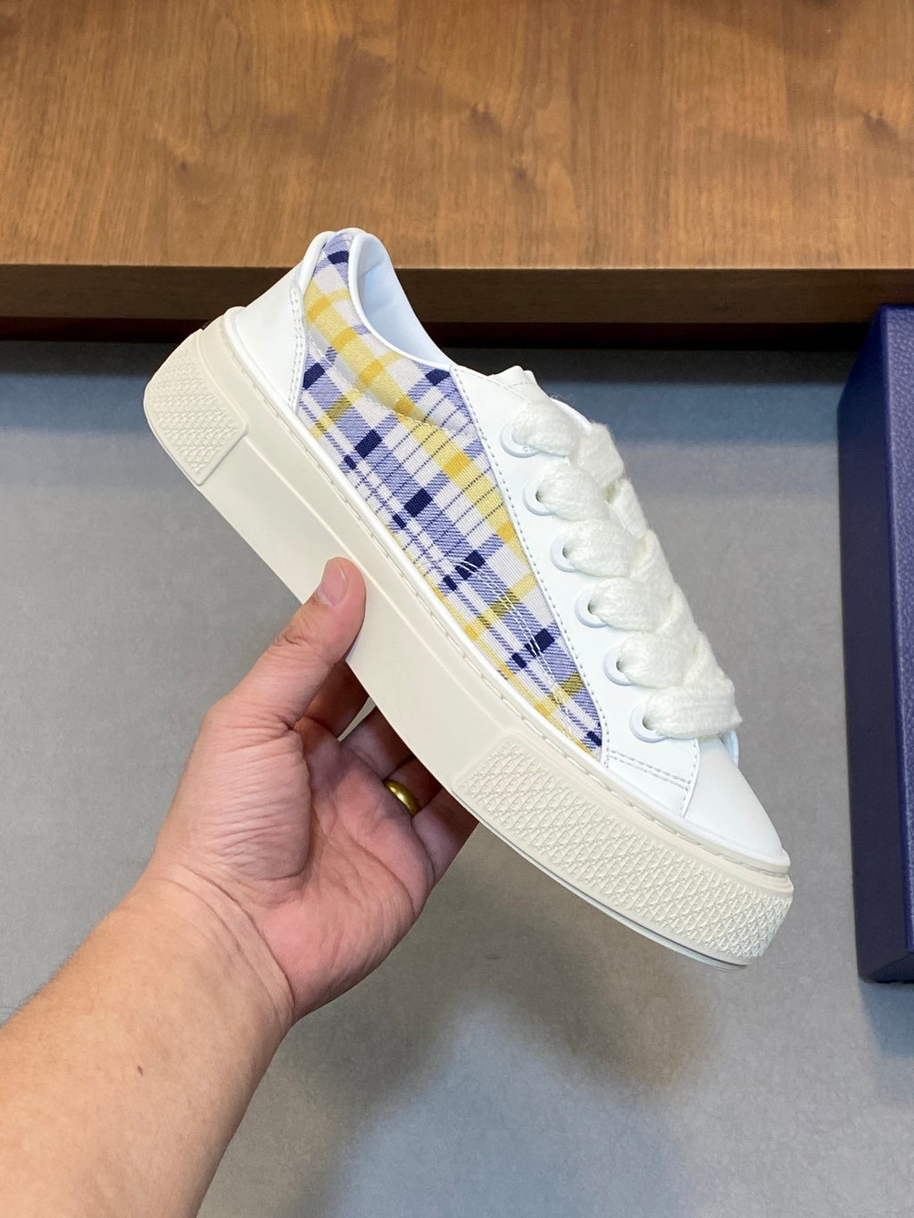 White low-top sneaker with blue yellow plaid stripe and lace-up closure.