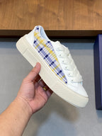White low-top sneaker with blue yellow plaid stripe and lace-up closure.