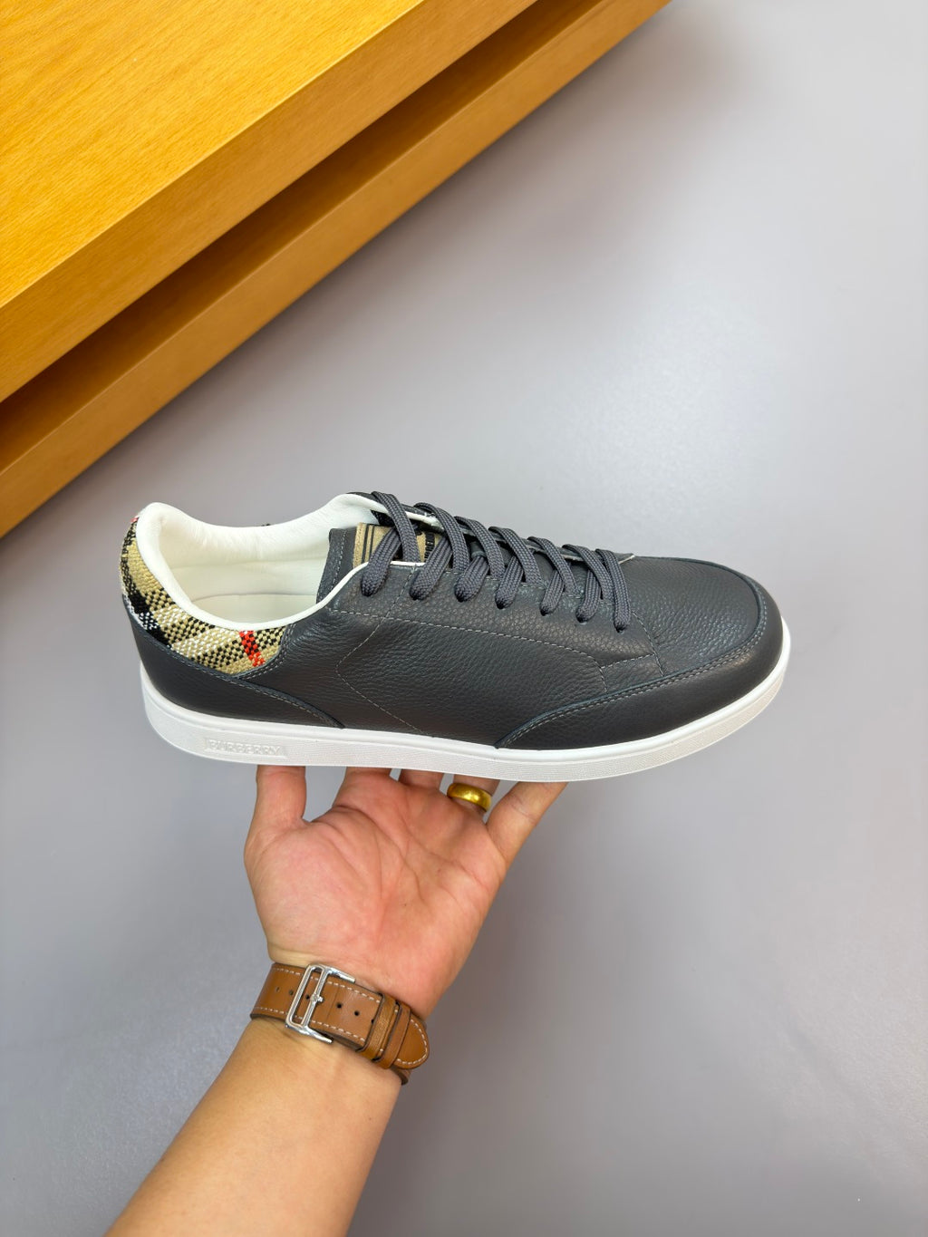Dark leather sneakers with white sole and blue-gray laces, held for close-up