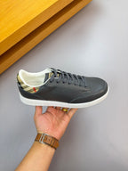 Dark leather sneakers with white sole and blue-gray laces, held for close-up
