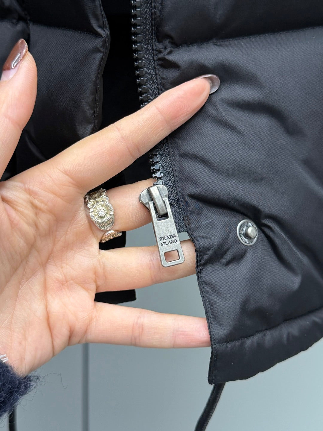 Black puffer jacket sleeve detail with PRADA logo patch and metal button