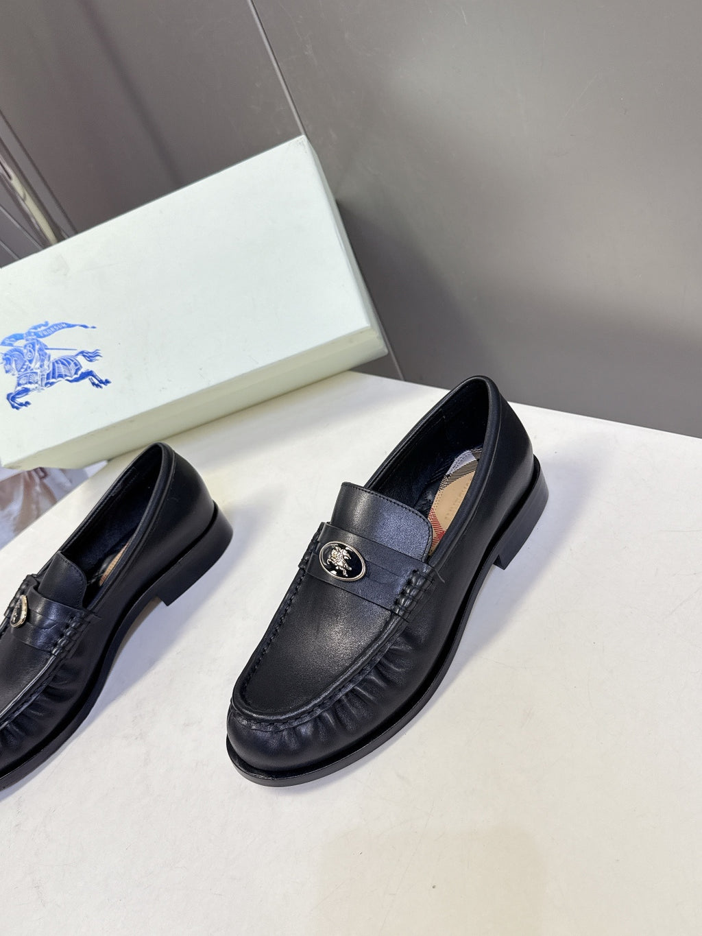 Burberry black leather loafers, front pair view with gold emblem on strap
