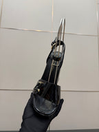 Black patent heeled sandal held in hand with ankle strap and buckle