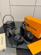Women’s platform heeled sandals, black leather, wide straps with V buckle details.