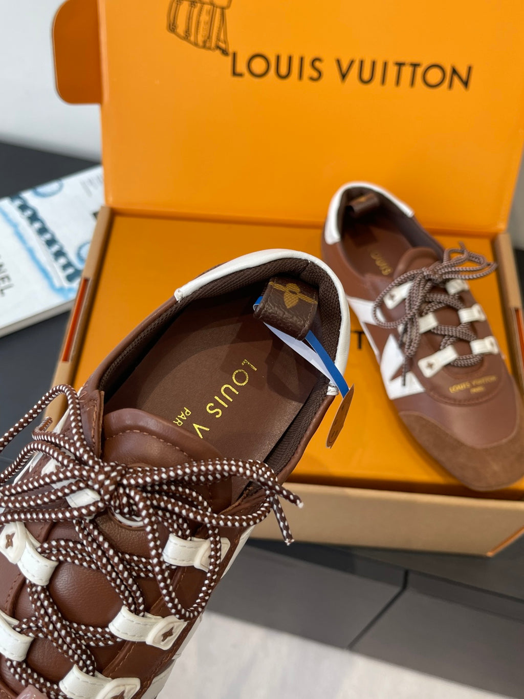 Brown sneakers with white side stripe, lace-up bows, and logo patch