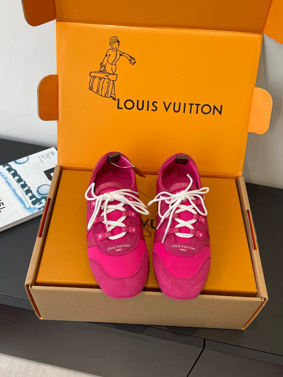 Unisex sneakers in bright pink with white lace-up front, shown in a box