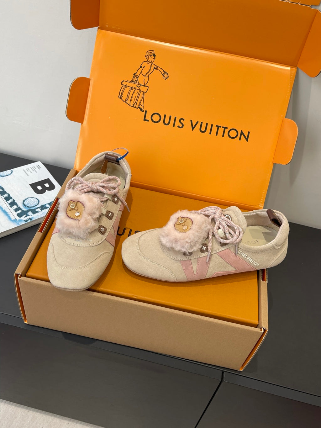 Pair of light beige suede sneakers with pink laces and fur trim, side view in box