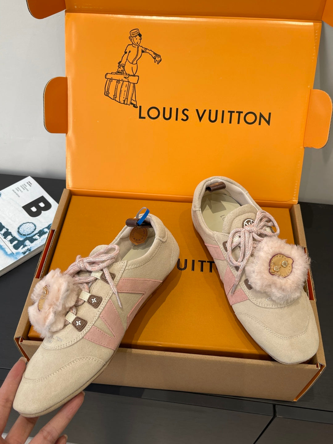 Pair of beige suede sneakers with pink laces and fur trim, angled view in box