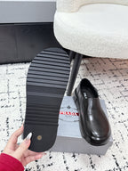 Black leather loafer outsole with horizontal tread; shoe beside box, PRADA logo