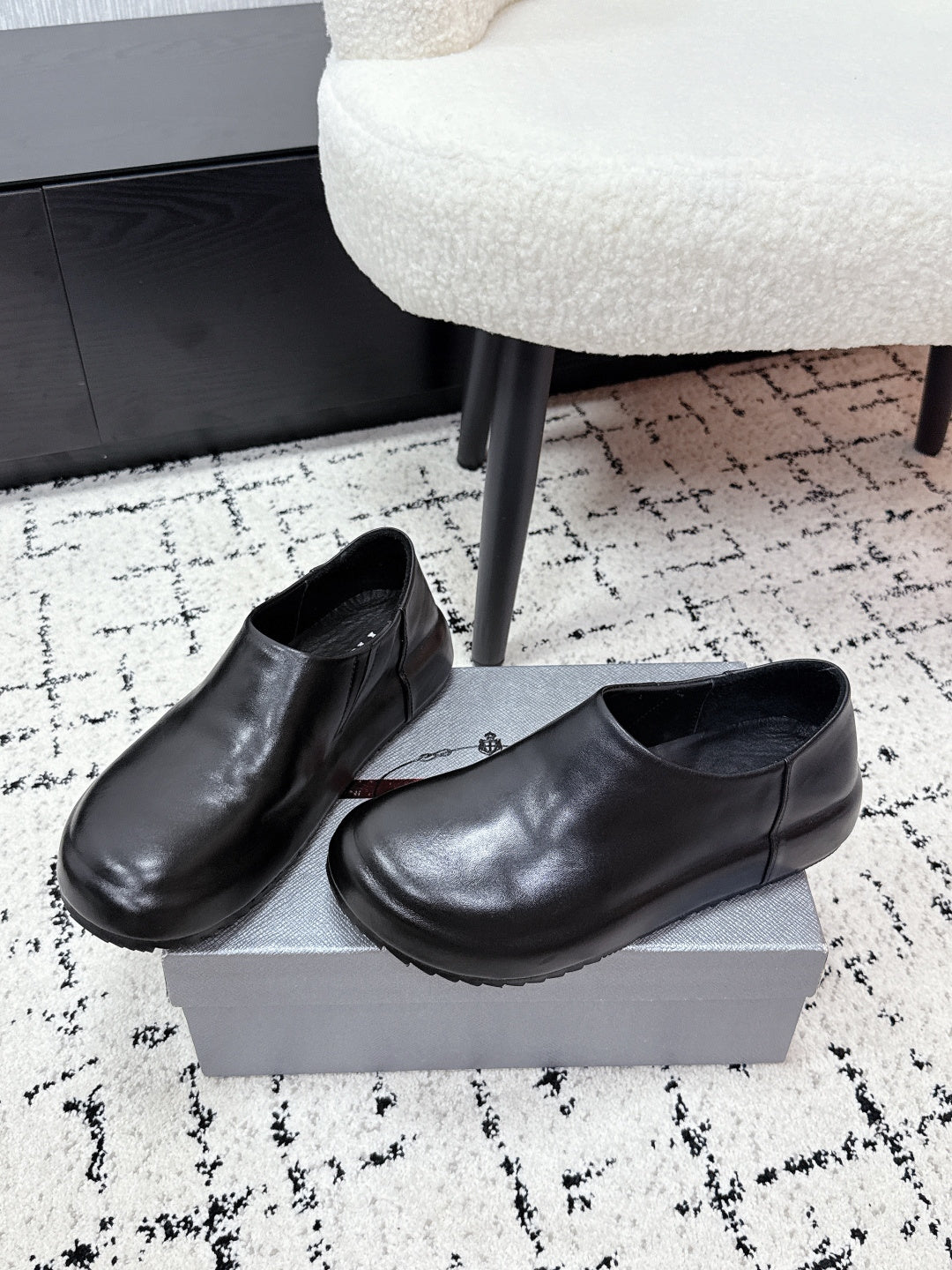 Pair of black leather loafers on a box, rounded toe and PRADA logo insole