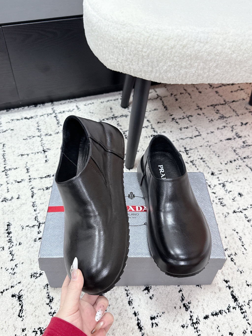 Black leather loafer pair with rounded toe, PRADA logo on insole; held by hand
