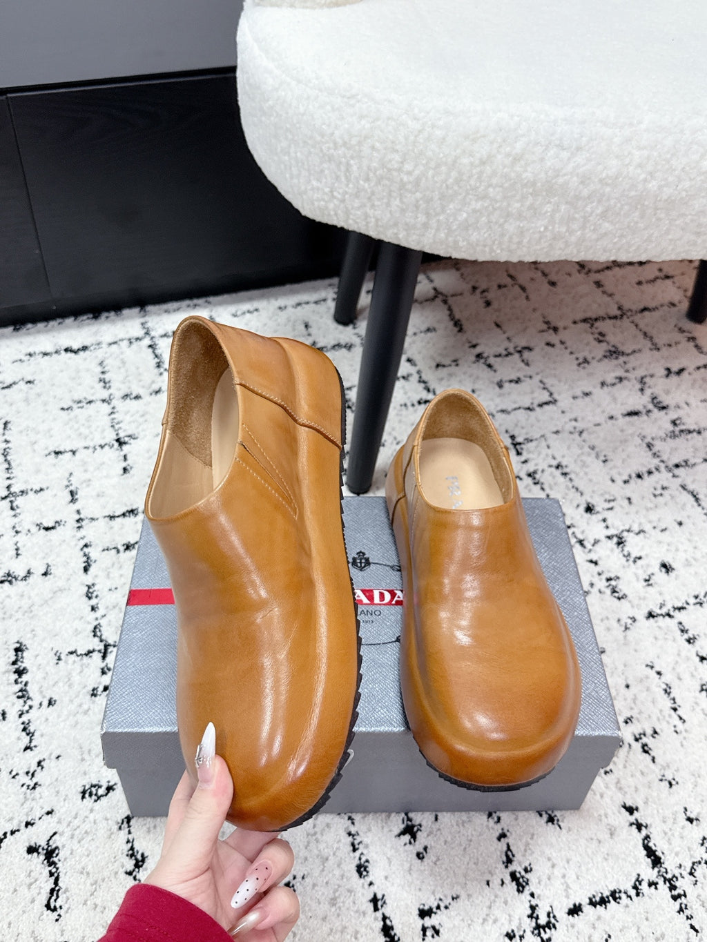 Brown leather slip-on loafers with rounded toe; PRADA tag visible.