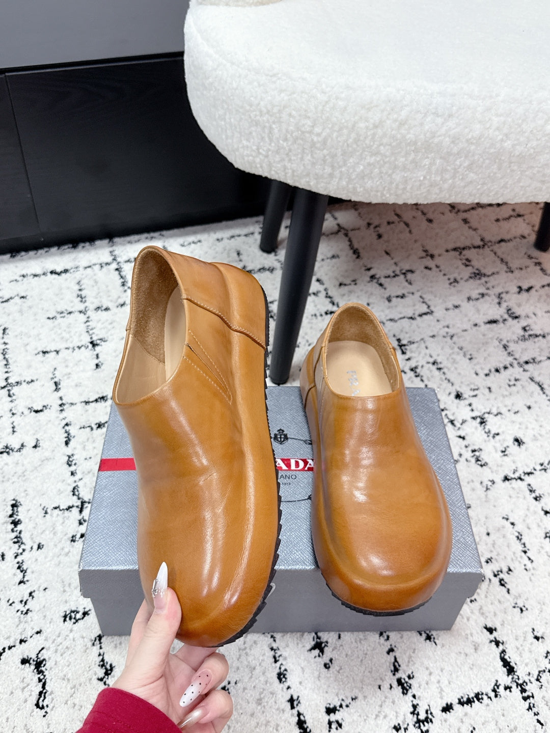 Brown leather slip-on loafers with rounded toe; PRADA tag visible.