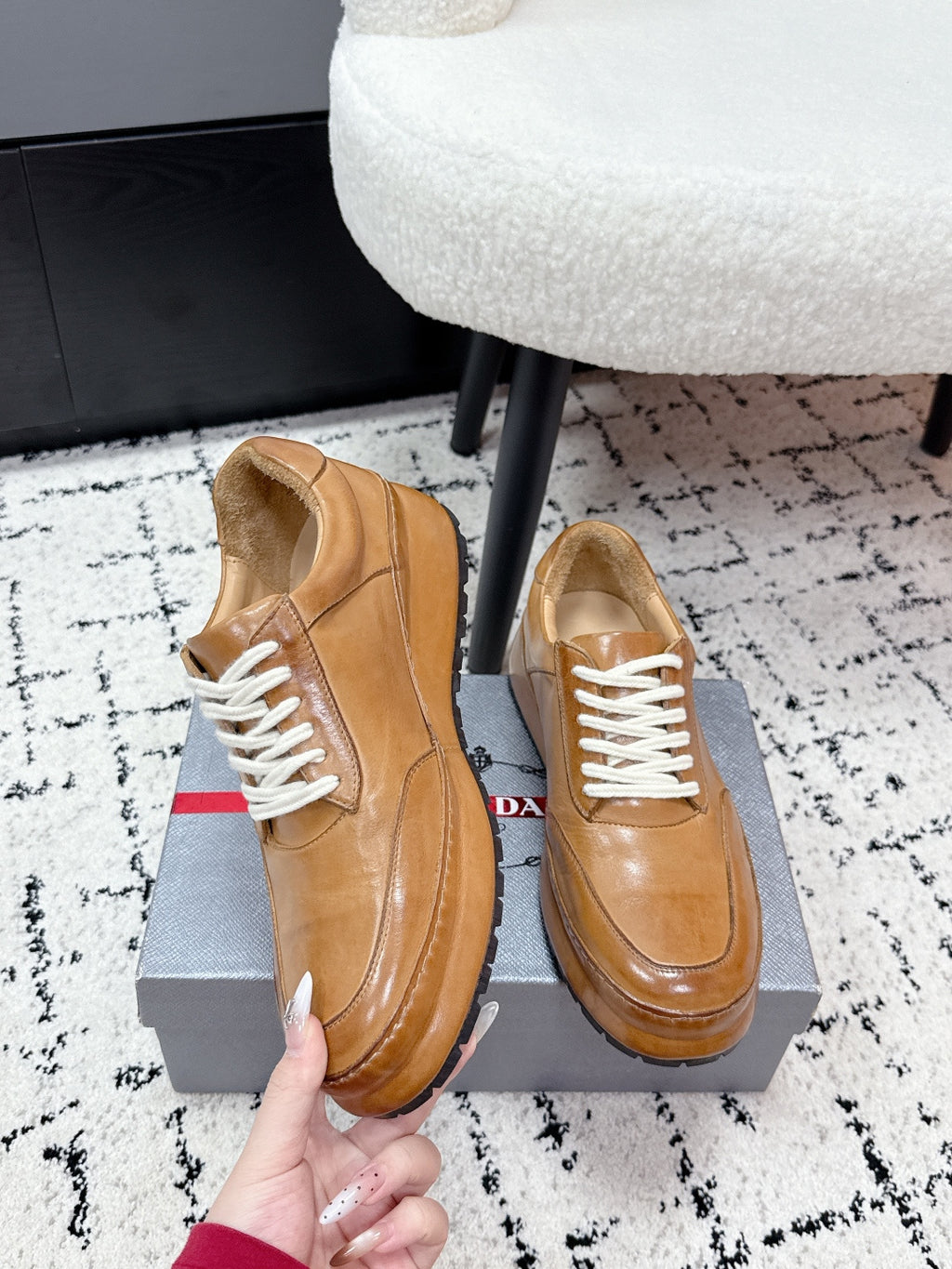 Tan unisex Prada leather sneakers, side view held by hand with white laces