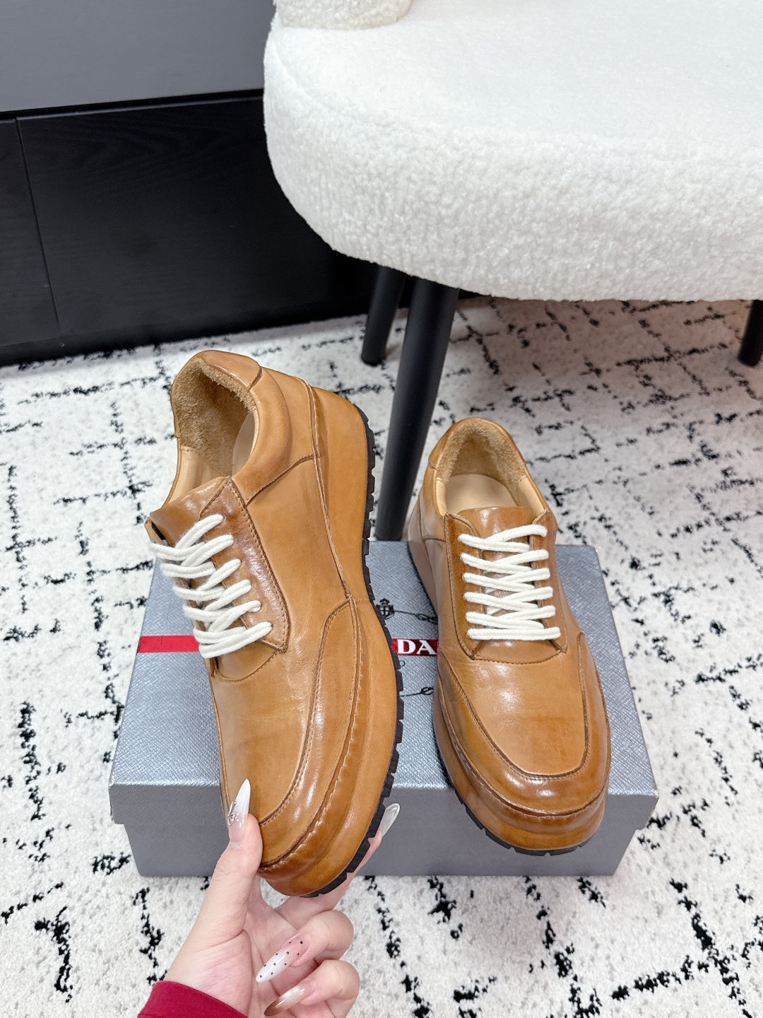 Tan unisex Prada leather sneakers, side view held by hand with white laces