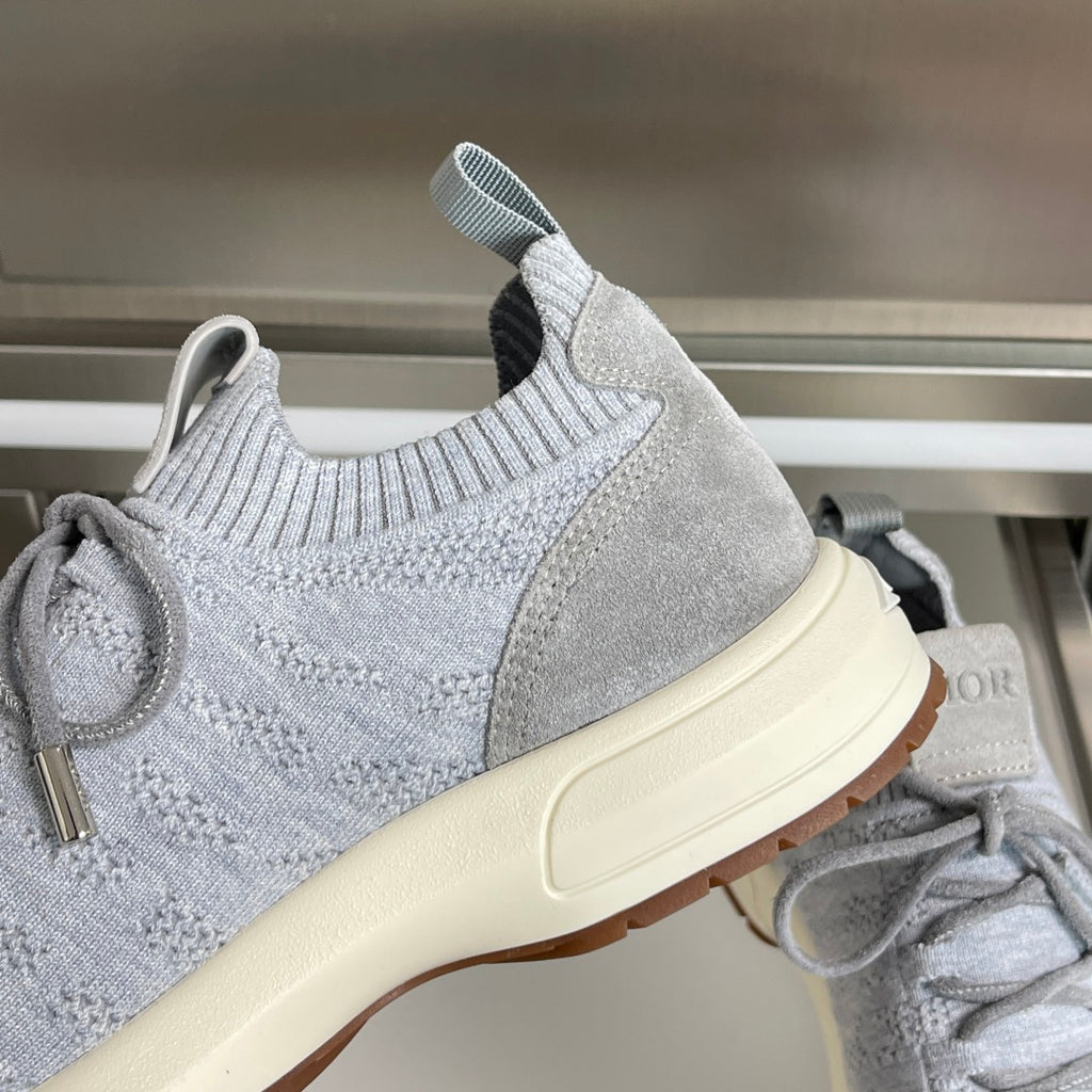 Close-up of light grey knit sneakers with elastic collar and cream sole, Dior branding