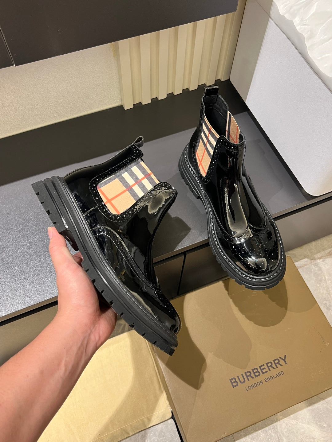 Burberry black patent Chelsea boots held by hand, showing elastic side detail