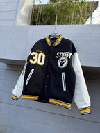 Varsity jacket in dark with yellow-and-white striped collar, front snap buttons, Stussy patches