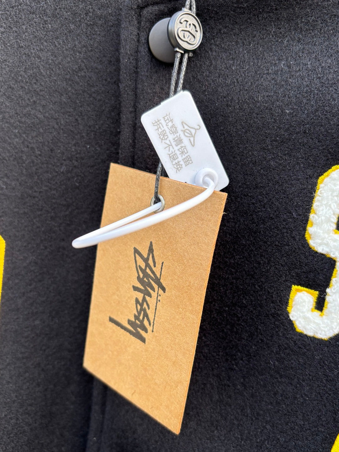 Black fleece jacket with yellow appliqued letter J and zipper pull tag
