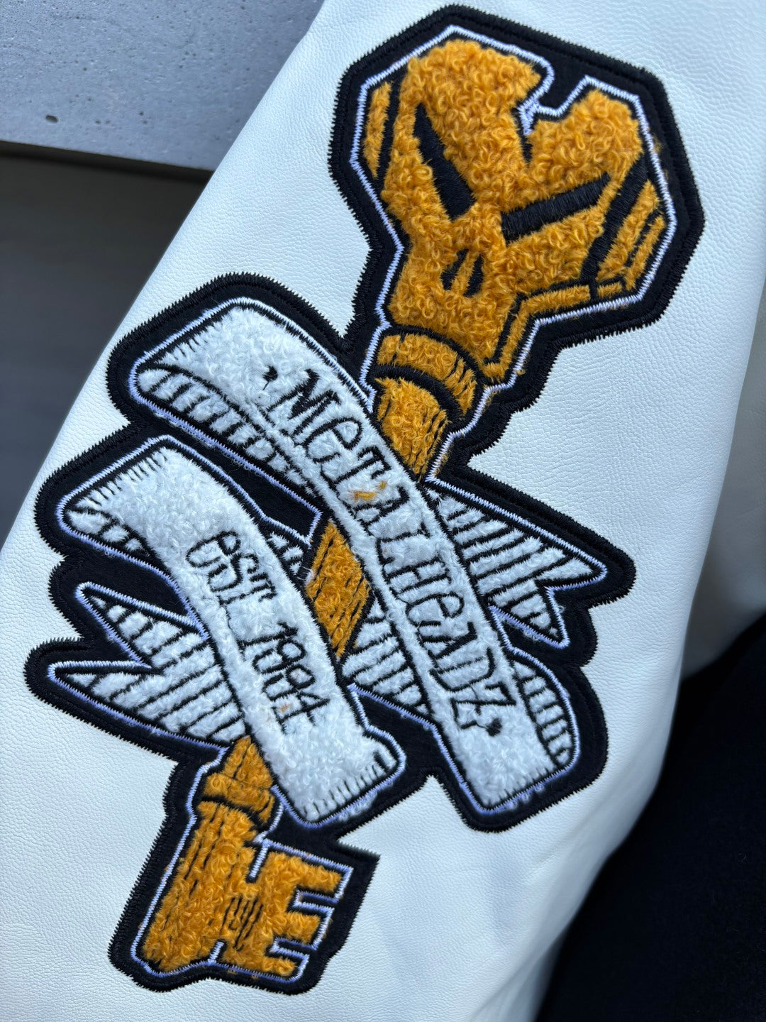 Varsity jacket sleeve patch close-up with yellow-and-white embroidery and stitched outlines