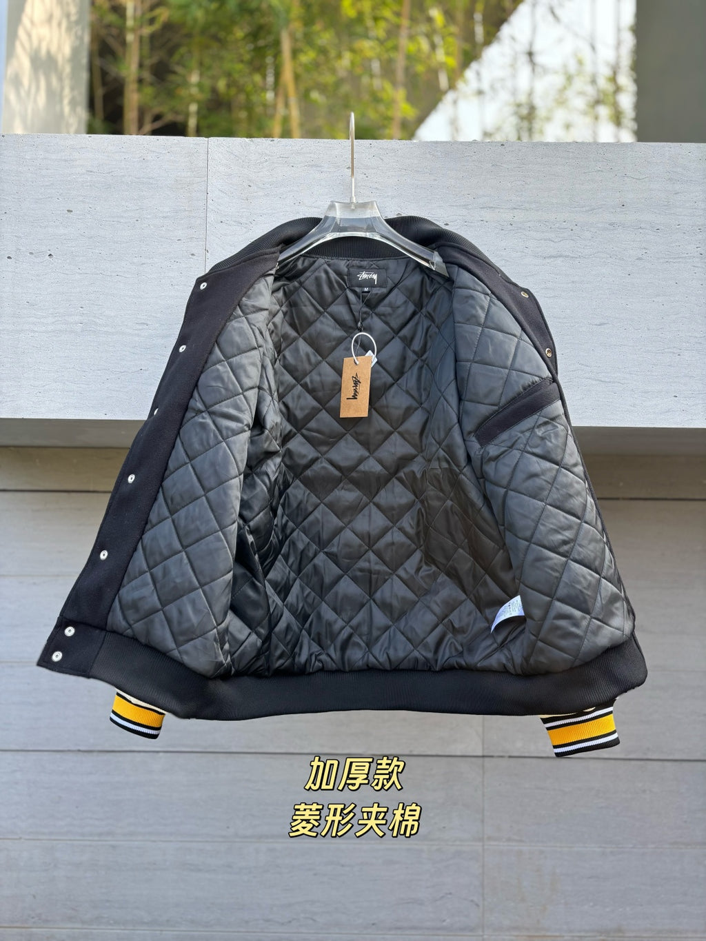 Quilted varsity jacket with dark gray body, black sleeves, snap front and hanging tag