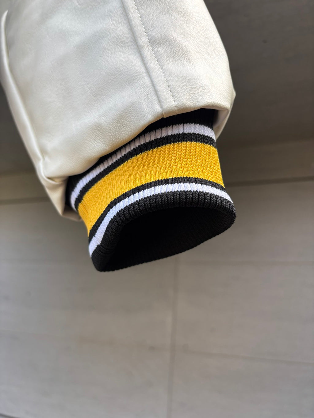 Varsity jacket sleeve cuff close-up with yellow center stripe and white-and-black rib trim