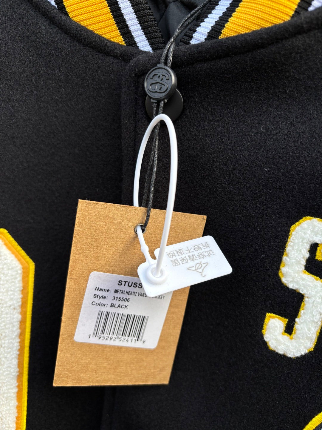 Varsity jacket neckline close-up with snap placket and hanging brand tags