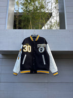 Varsity jacket with black body, white sleeves, yellow striped cuffs, snap button front