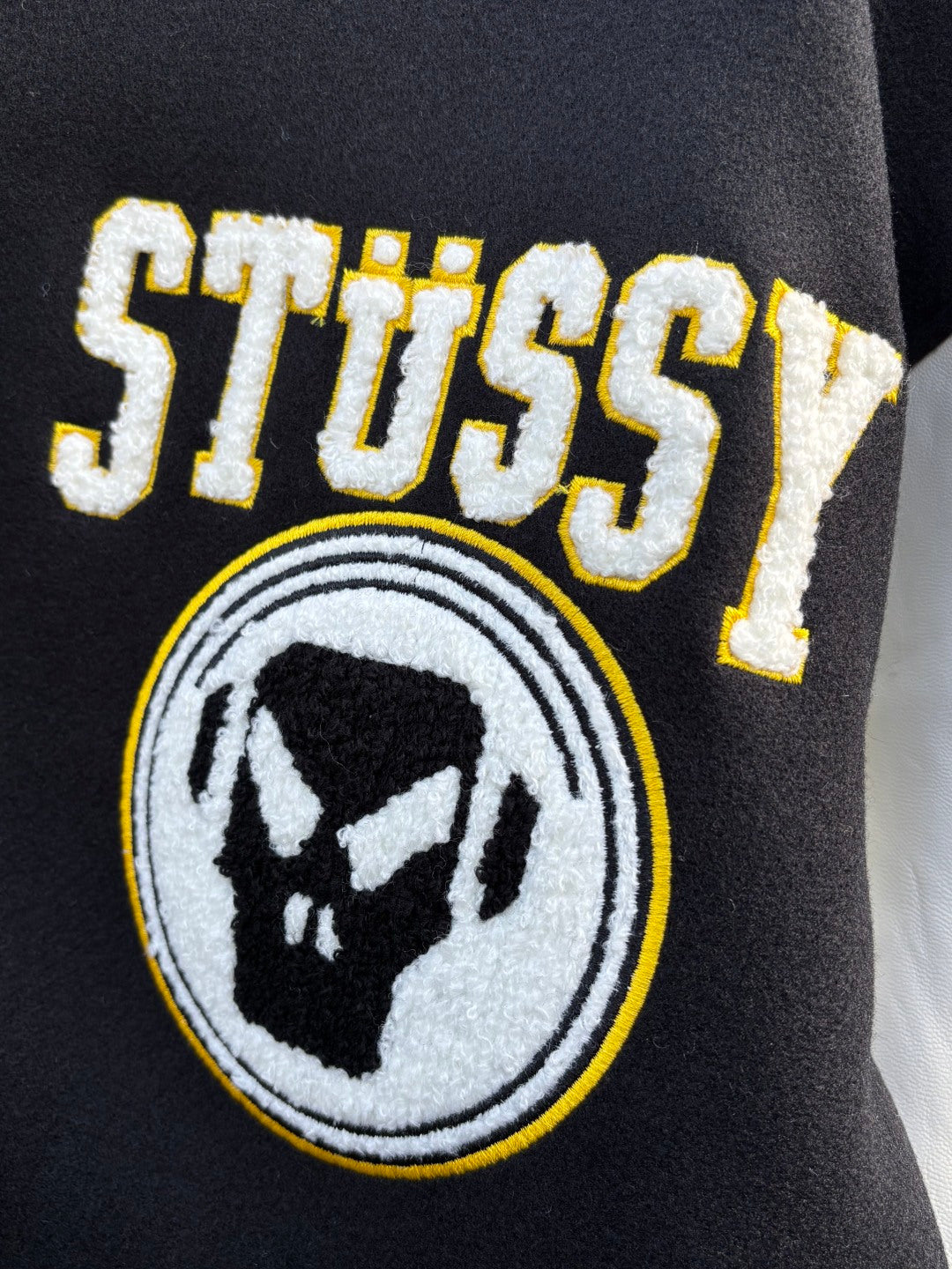Black varsity jacket embroidered Stussy logo patch and bear emblem