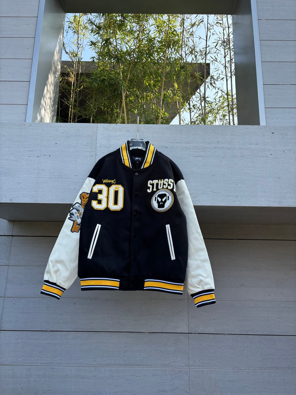 Black varsity jacket with white sleeves, yellow trim, STUSSY patch and 30 emblem